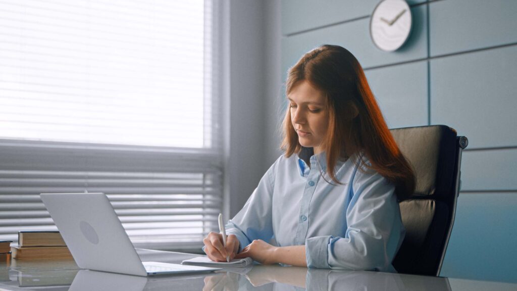 young woman writing on a paper in front of a computer