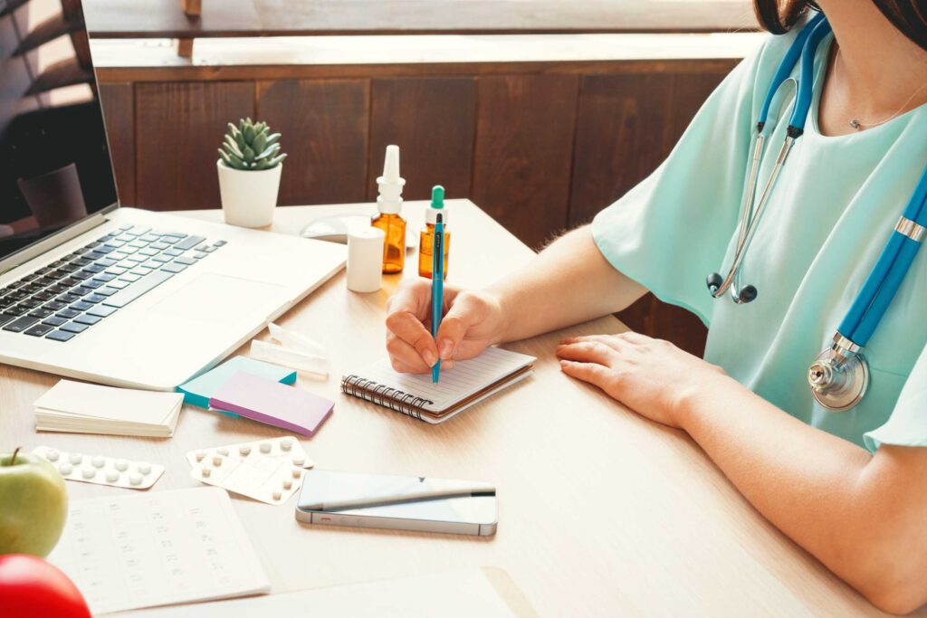 medical professional taking notes in front of a laptop